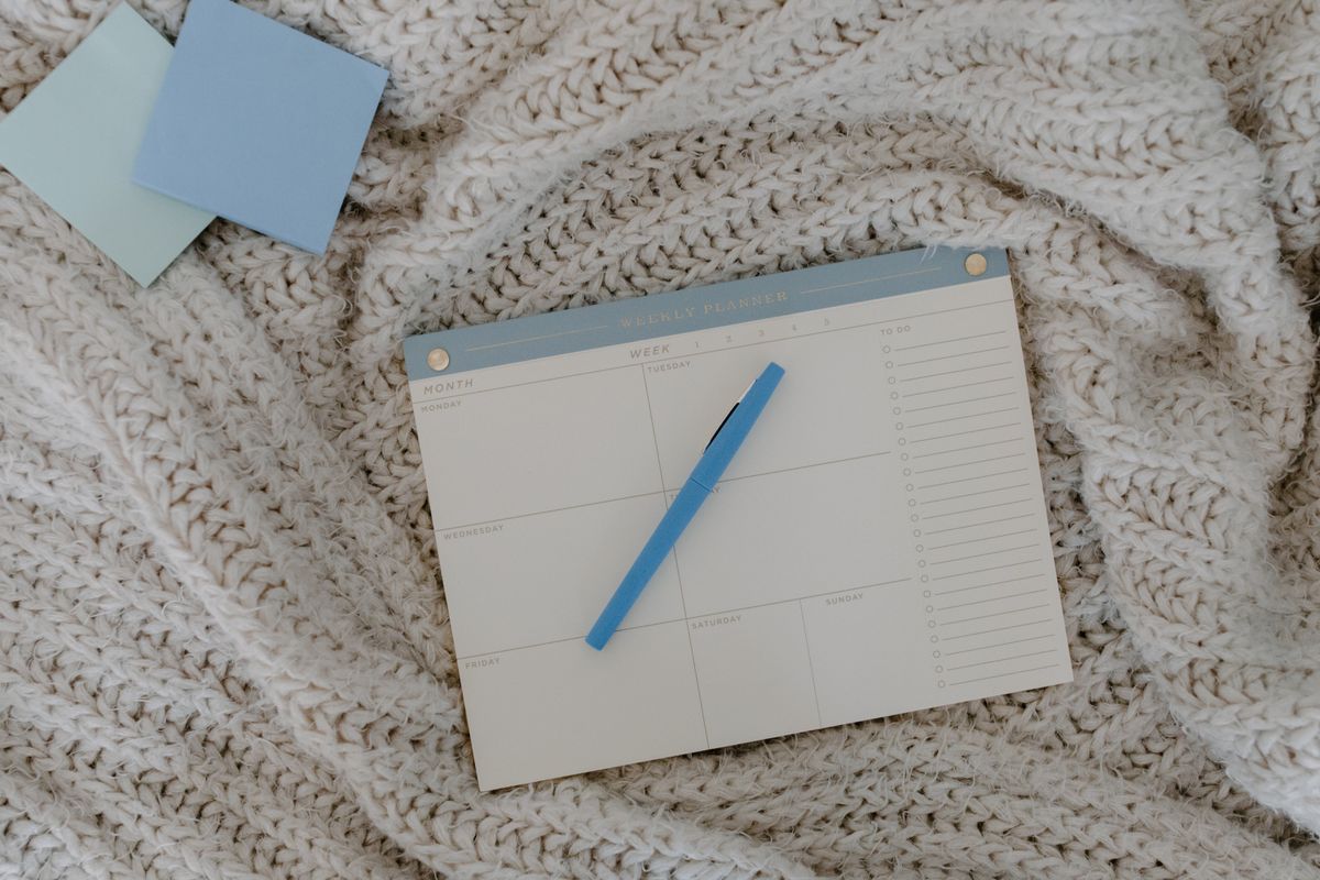 A weekly planner and a pen resting on a knitted blanket.